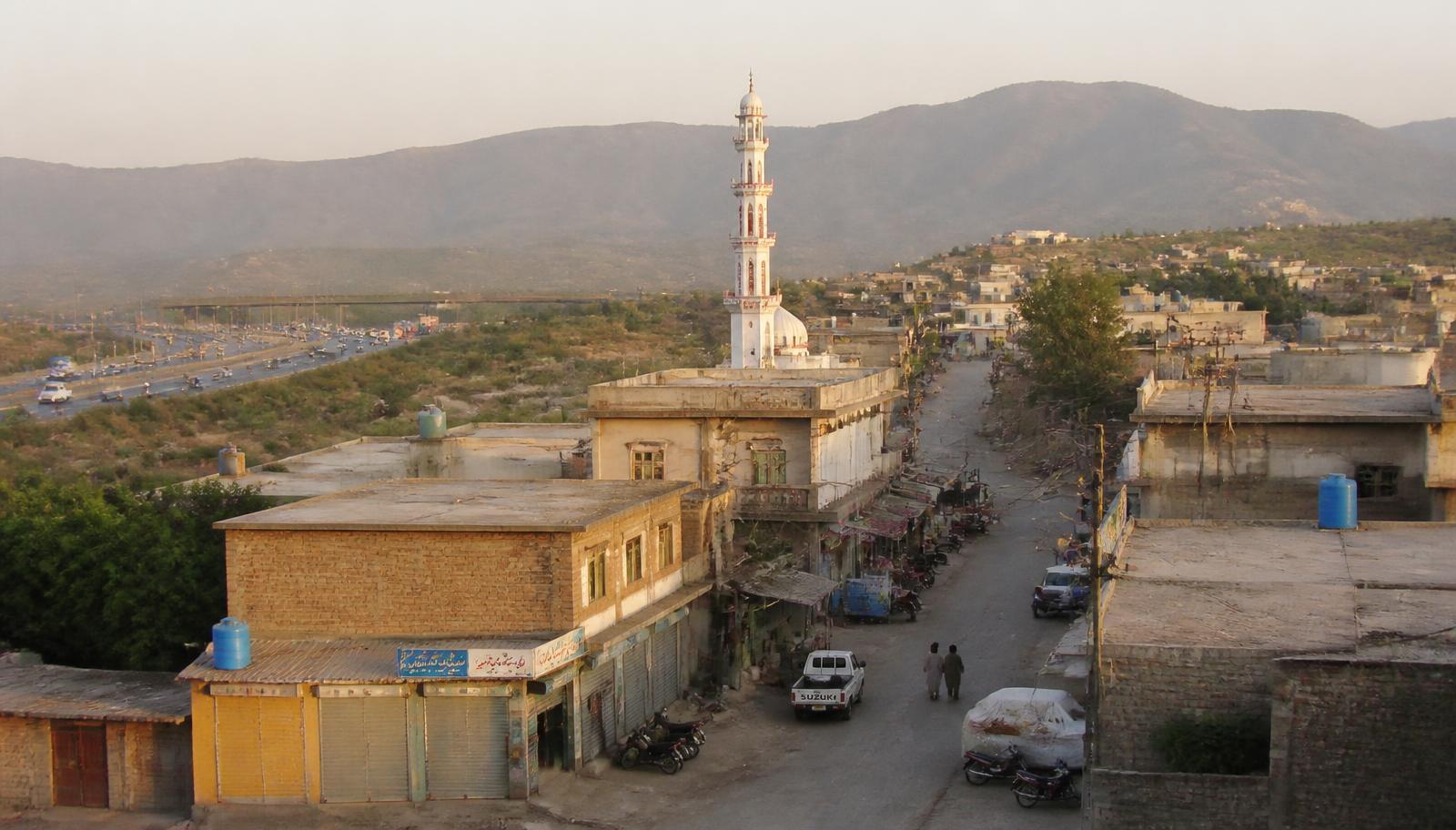 سوہان اسلام آباد کی گلی کا منظر: کنکریٹ کے مکانات، چھوٹی دکانیں اور قریب سے گزرتی اسلام آباد ایکسپریس وے